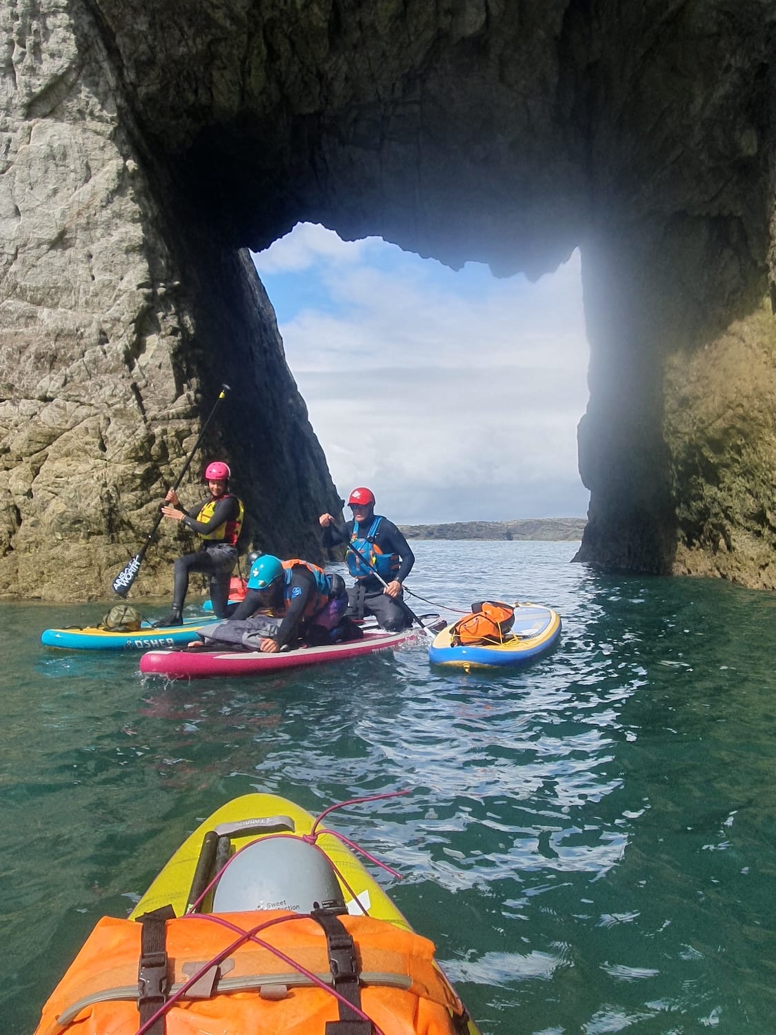 Outdoor instructors practicing paddleboard rescues on the sea in a natural sea arch.