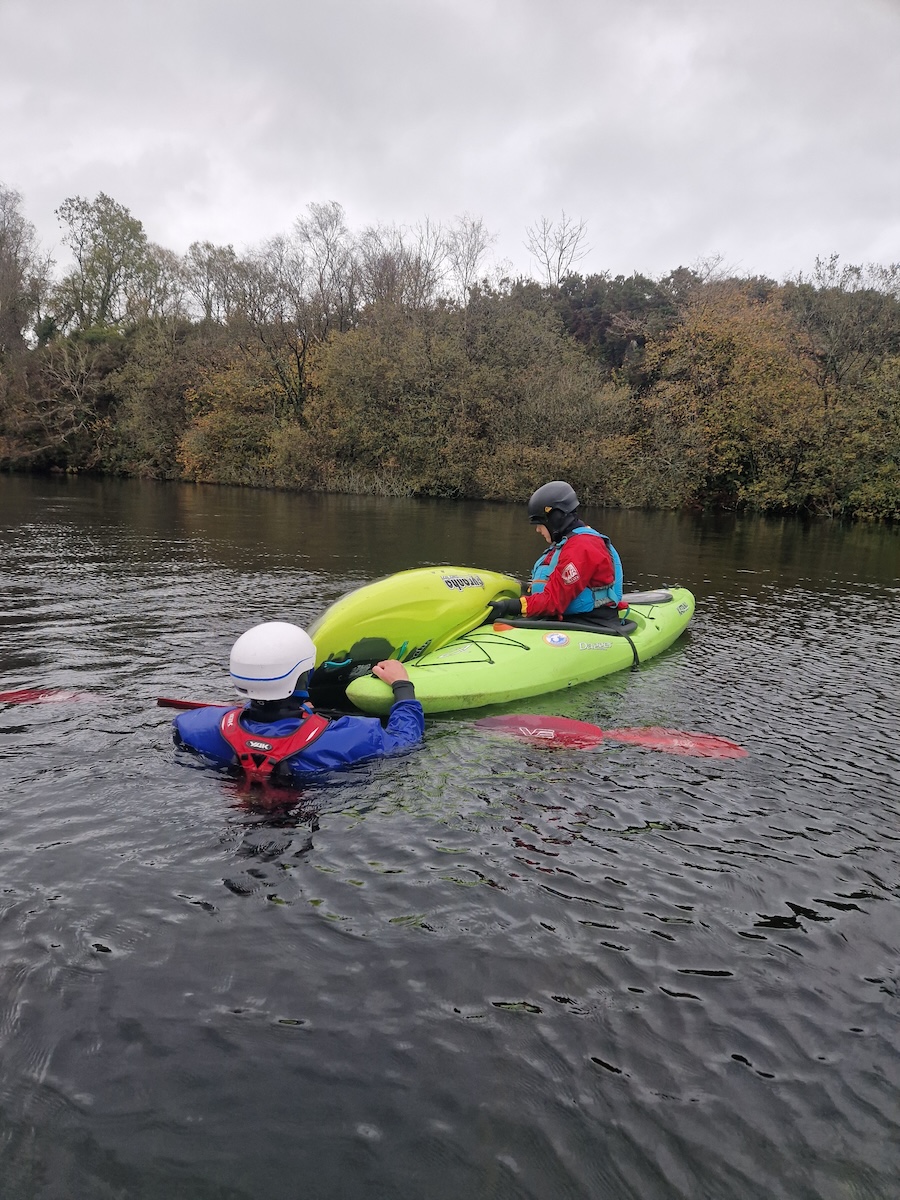 Outdoor instructor training students practising kayak safety and rescue skills on a river