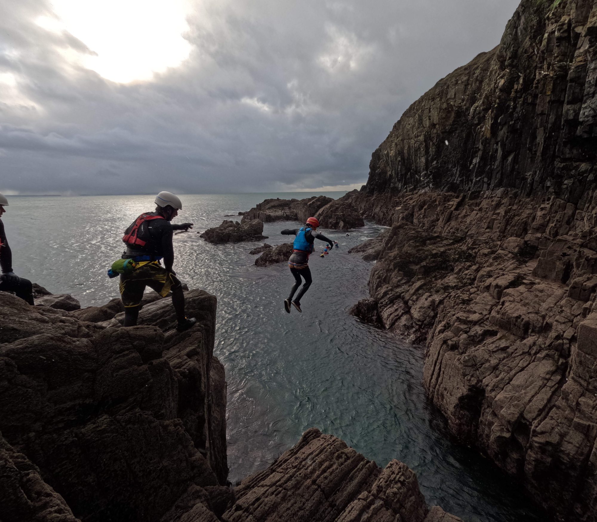 Outdoor instructor trainee jumping into the sea during a coasteering session between rocky cliffs