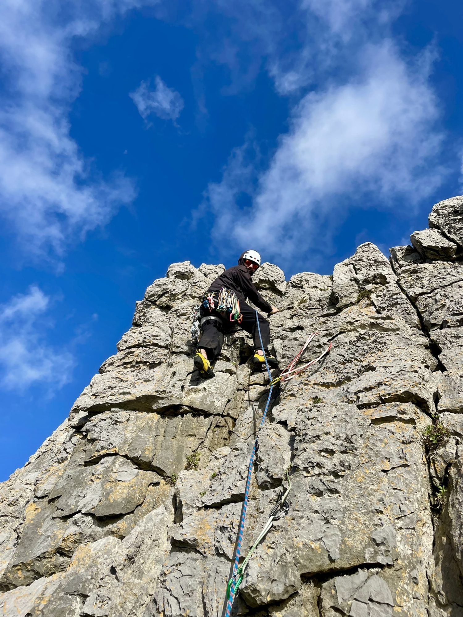 Outdoor instructor trainee leading a rock climb on a limestone cliff during professional training.