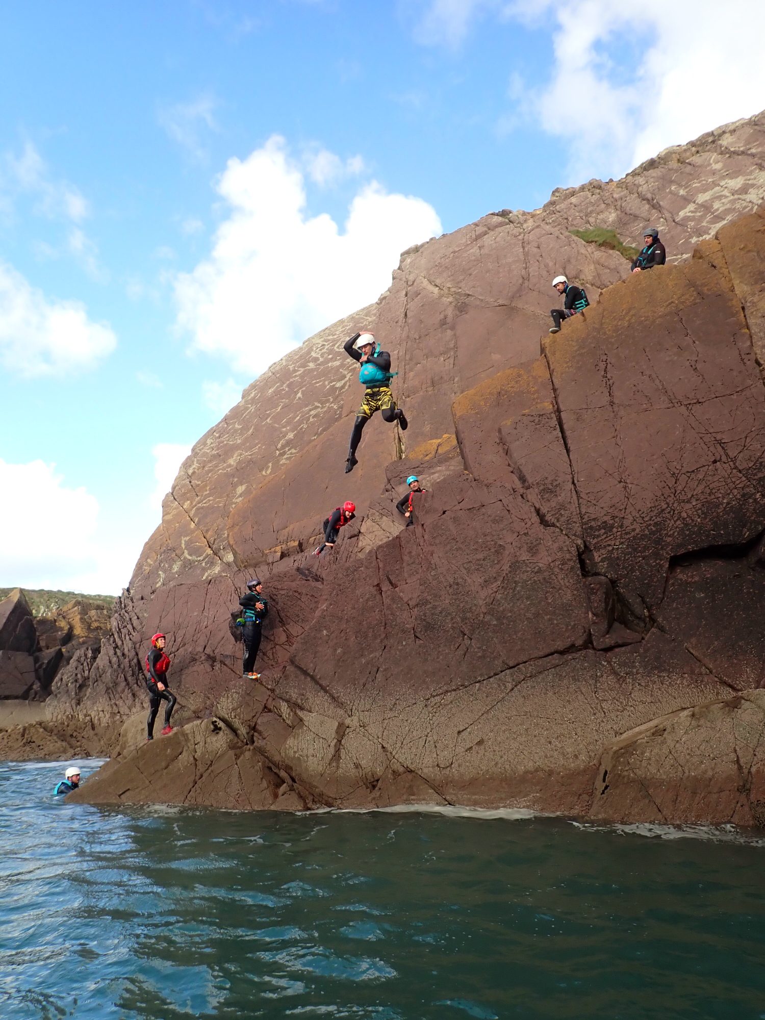 Outdoor instructor trainees coasteering, jumping from a rocky ledge into the sea under supervision